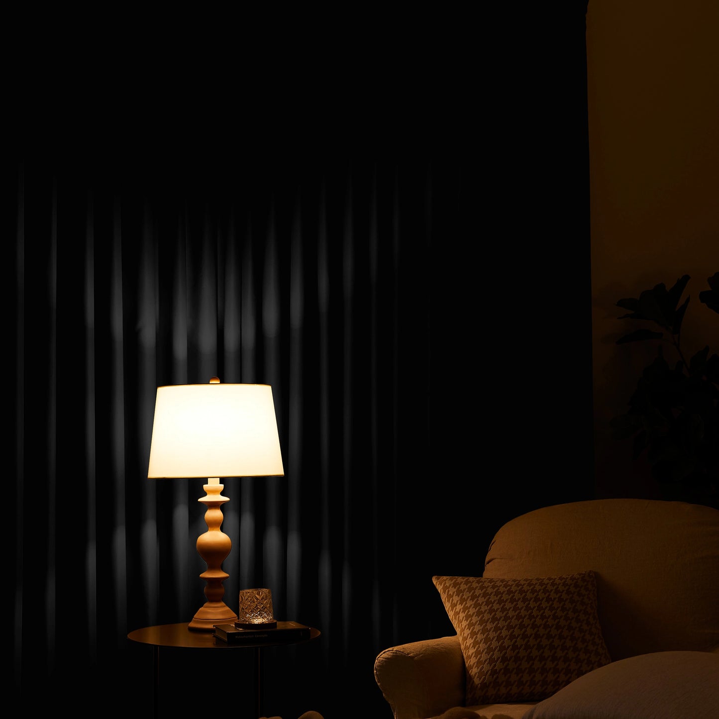Lamp on a table next to a chair with a jet curtain in the background