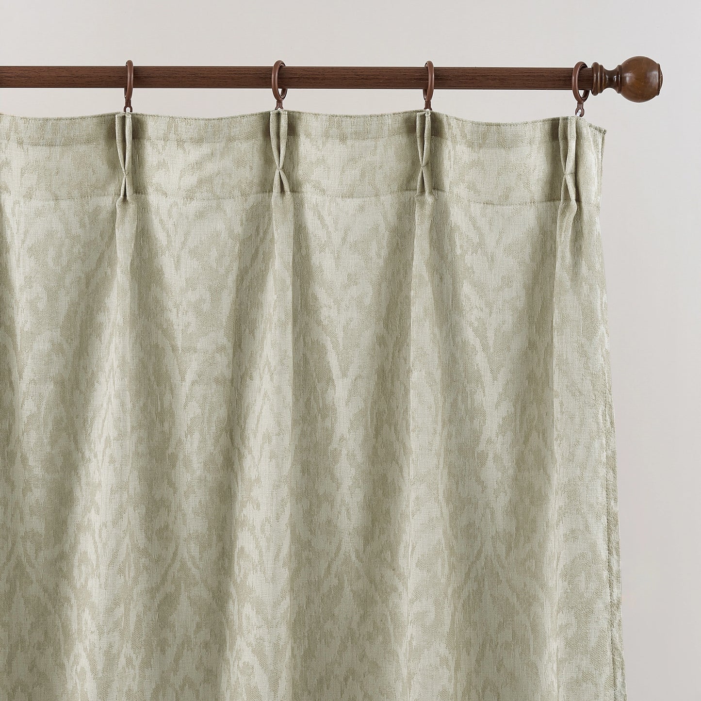 Textured green curtain hanging on a wooden rod against a white background