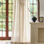 Taupe wool gauze curtain with subtle tone-on-tone embossed foliage pattern, in front of large window with vase on mantel.