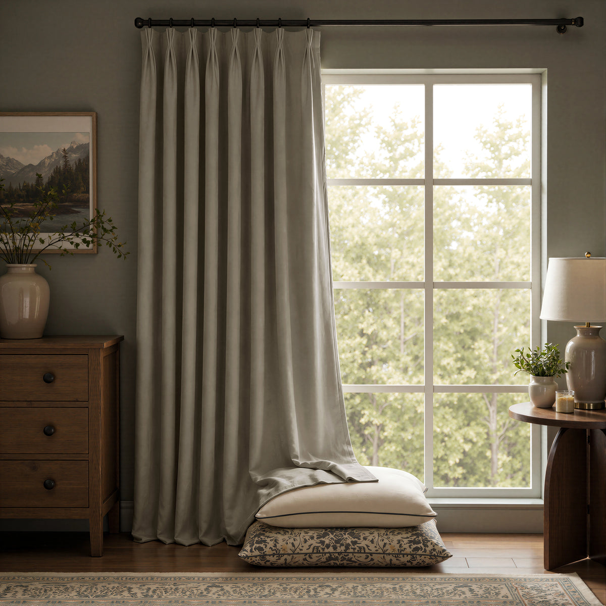 A pair of light sage green curtain panels hanging on a black rod in a styled room with a window, wooden furniture, and a lamp.