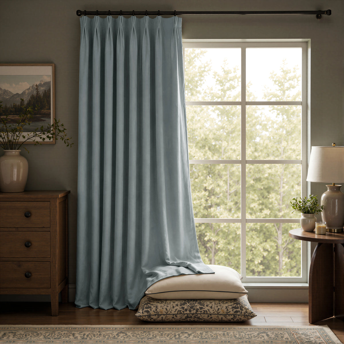 A light blue curtain panel hanging on a dark rod in a styled room with a large window, wooden furniture, a lamp, and pillows on the floor.