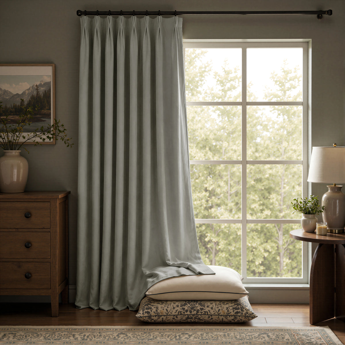 A pair of light sage green curtain panels hanging on a black rod in a styled room with a window, wooden furniture, and a lamp.
