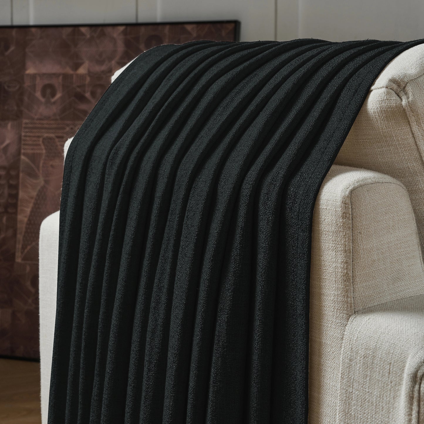 Textured black curtain draped over a sofa, with a decorative wall in the background.