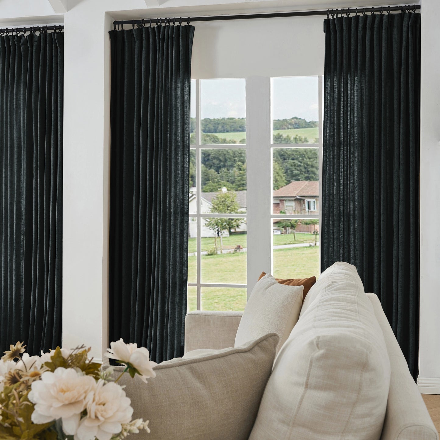 Living room with matte black curtains made of viscose, polyester, and linen, a sofa, and a view of greenery outside.