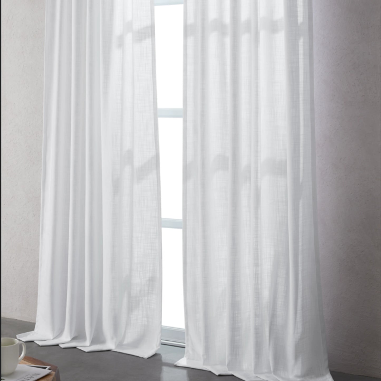 Bleached white linen-polyester blend curtains hanging in front of a window with a neutral background.