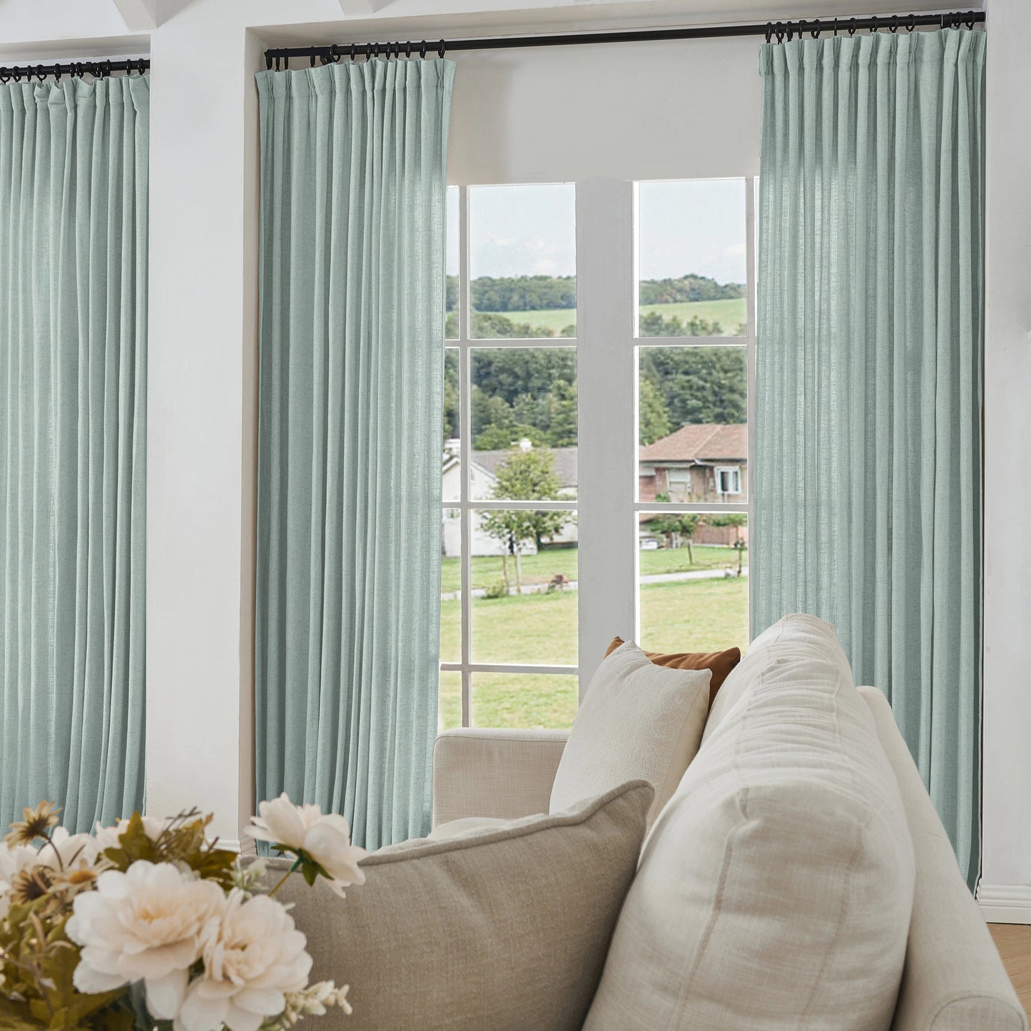 Living room with light blue curtains made of viscose, polyester, and linen, a sofa, and a view of greenery outside.