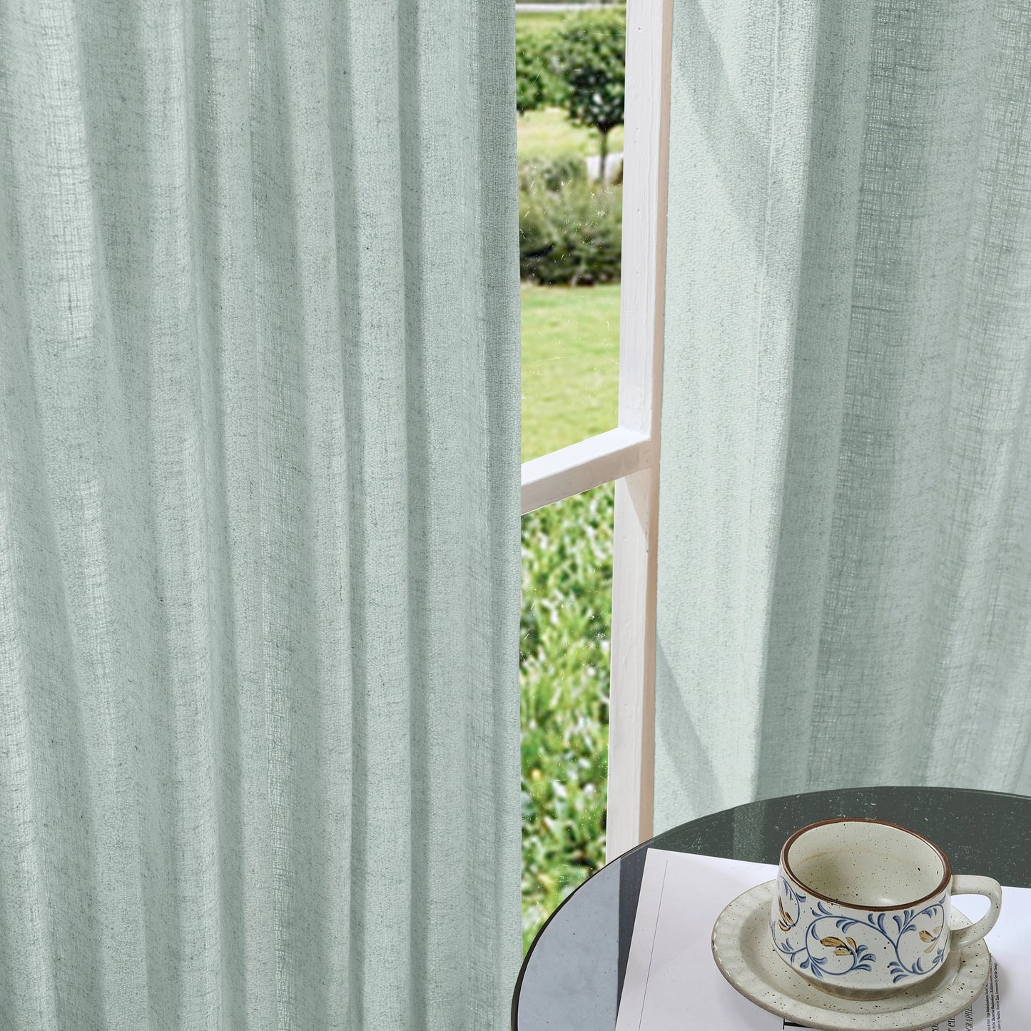 Soft slate blue curtains made of viscose, polyester, and linen, with a cup and saucer on a table in the foreground.