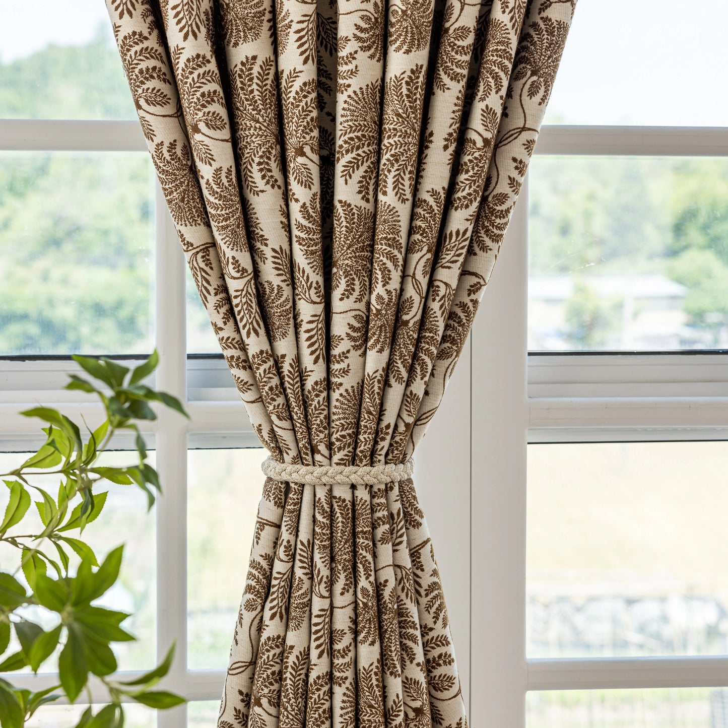 Bohemian taupe fern curtain hanging in front of a window with a view of greenery.
