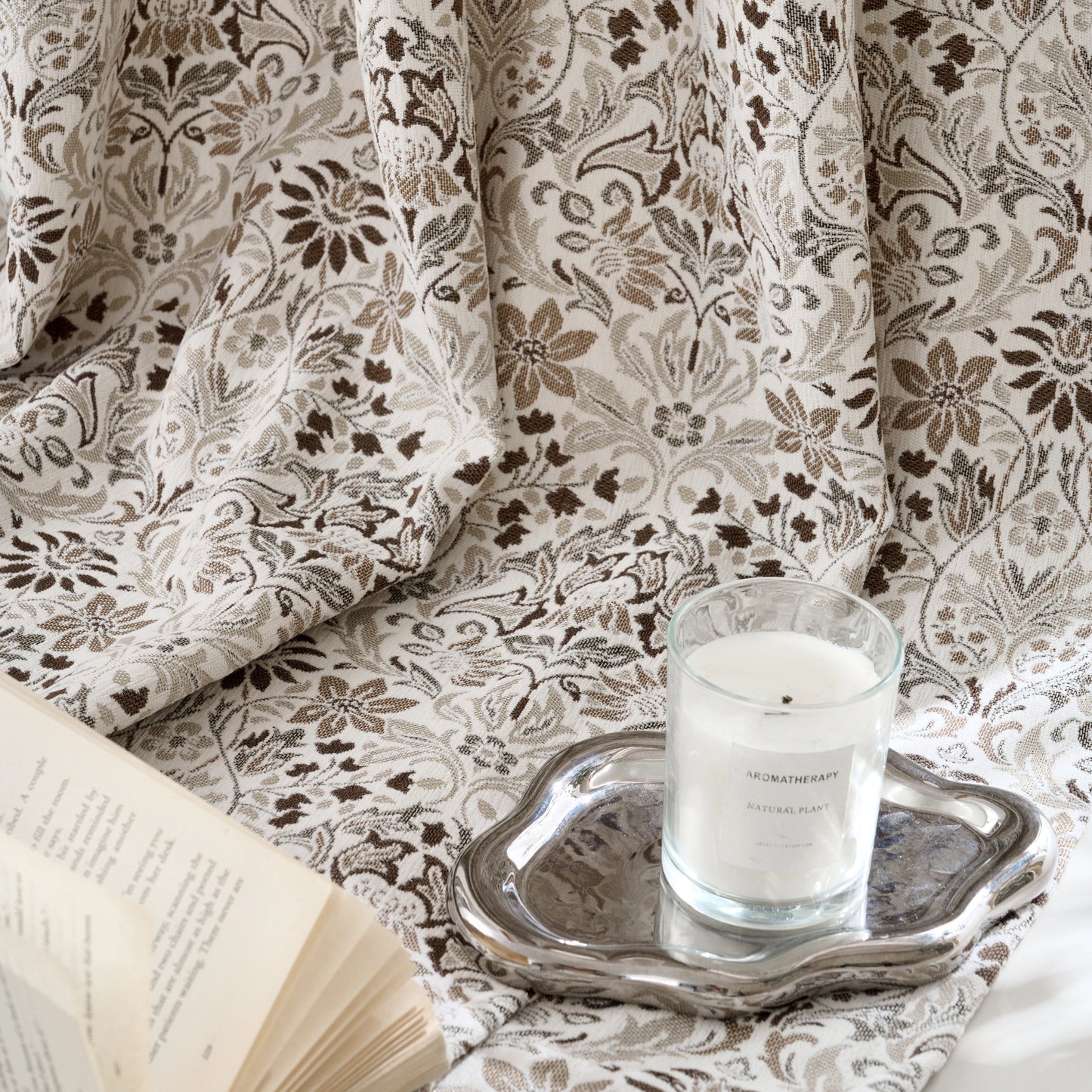 Close-up of a boho brown floral curtain with a book and an aromatherapy candle in the scene.