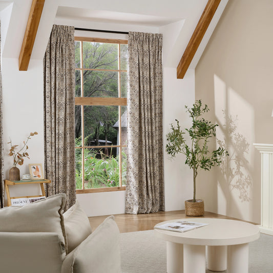 Living room with large window, patterned brown-toned boho floral curtains, and a small table with decor items.
