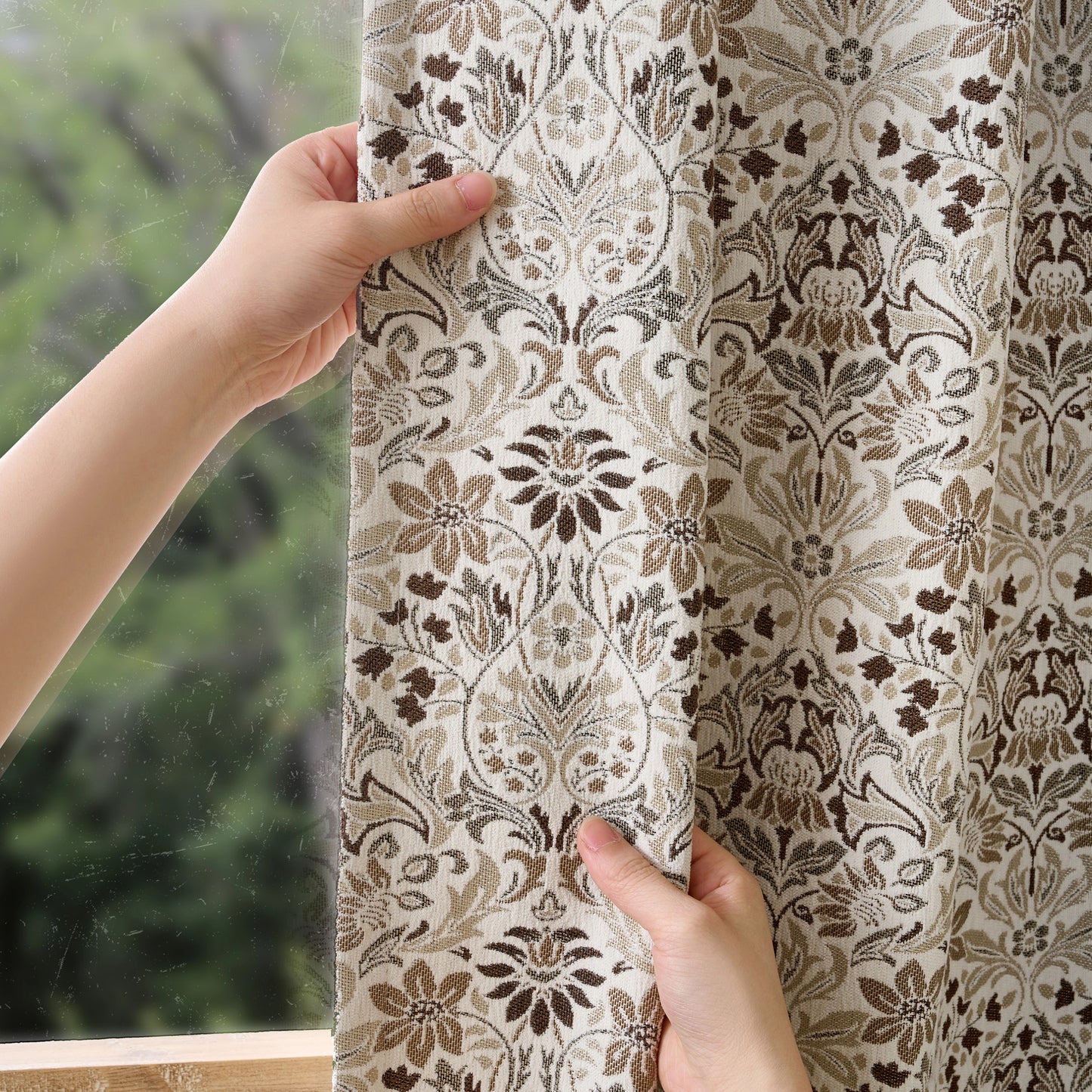 Hands holding a boho brown floral curtain in front of a window.