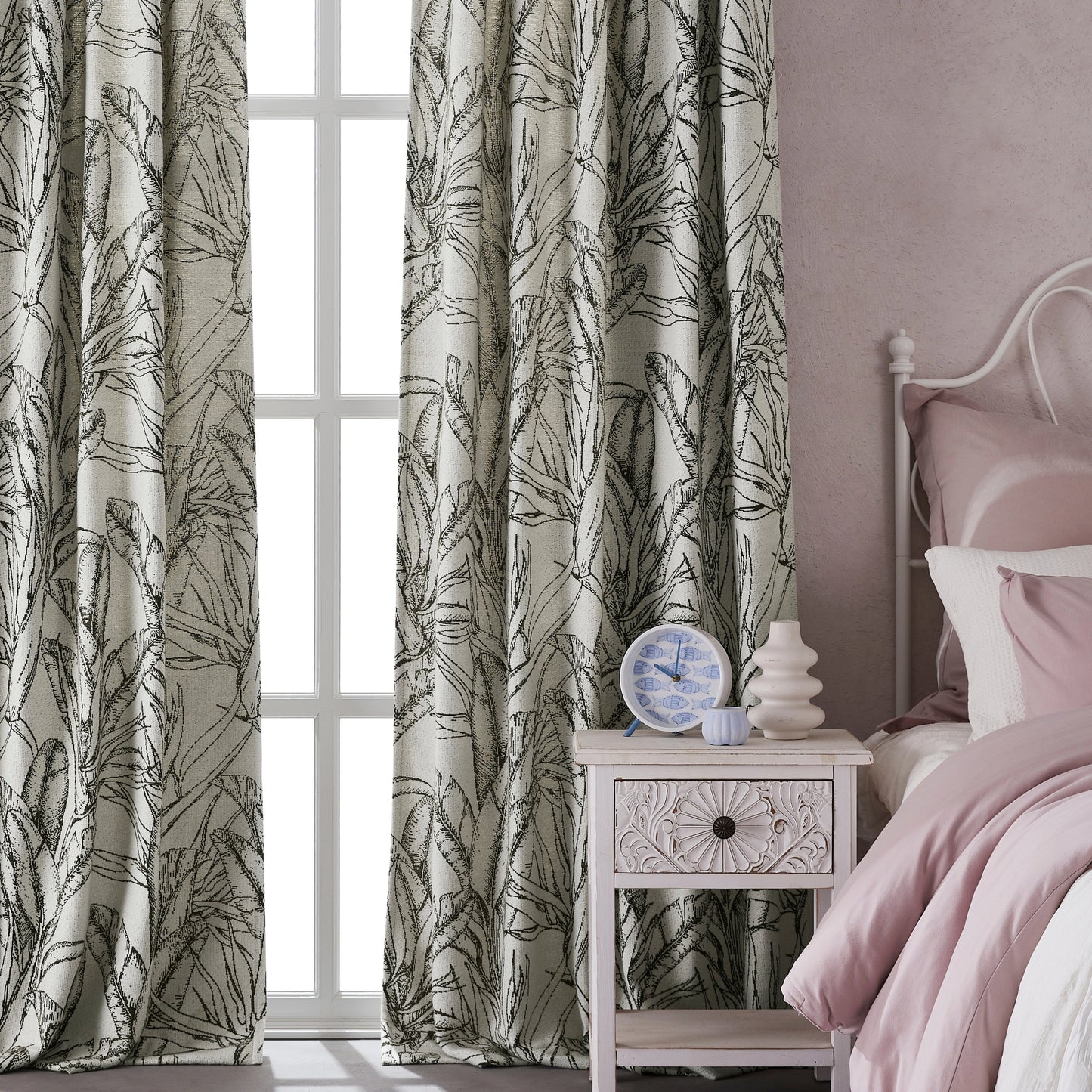 Bedroom with boho curtains featuring leafy sketch design in green tones, with a bed and nightstand in front.
