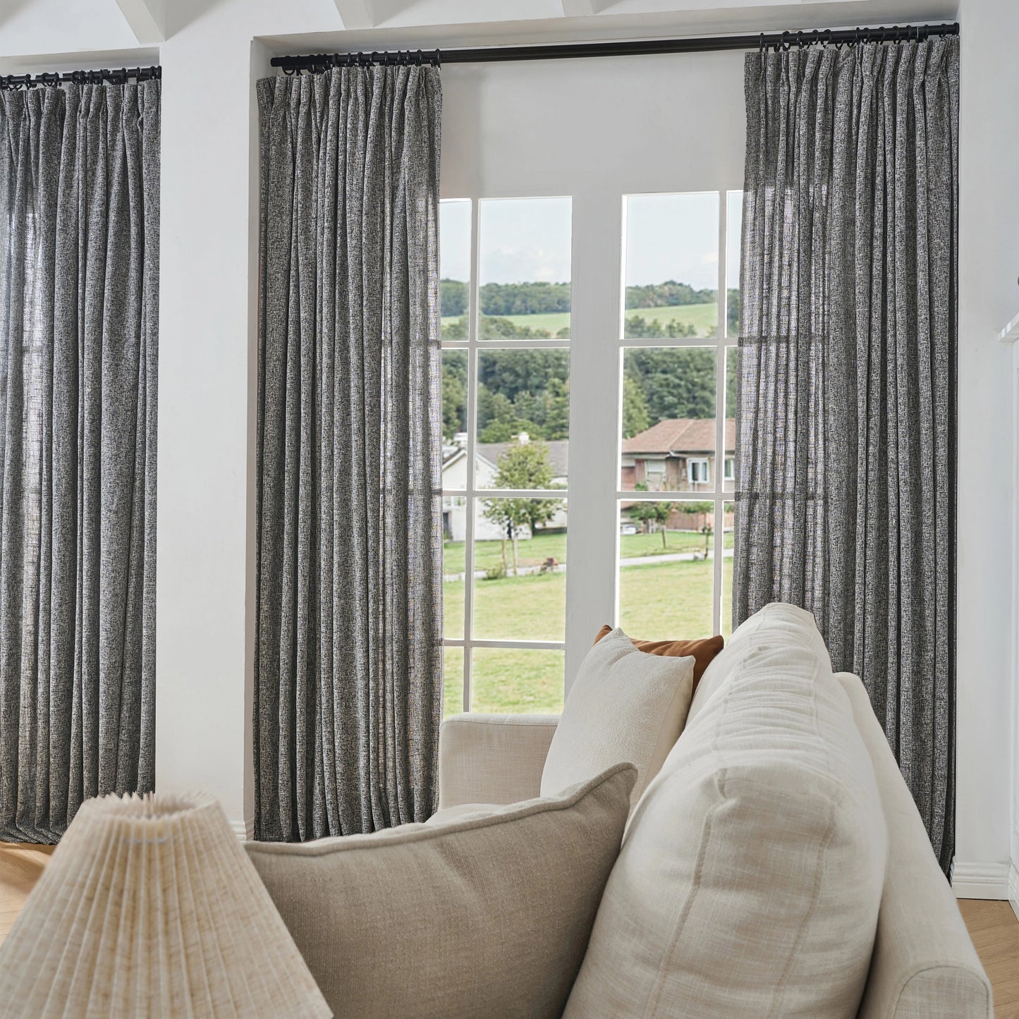 Black and off-white poly viscose linen window drapes, soft curtains and a sofa in a room with a large window view.