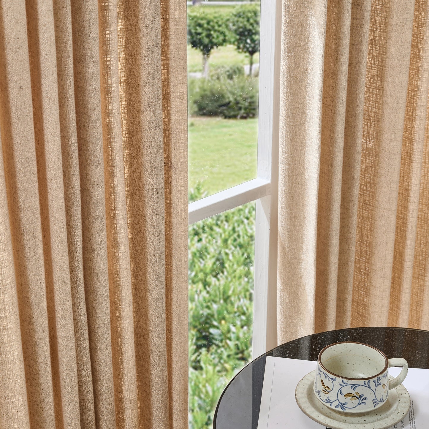 Soft camel curtains made of viscose, polyester, and linen, with a cup and saucer on a table in the foreground.