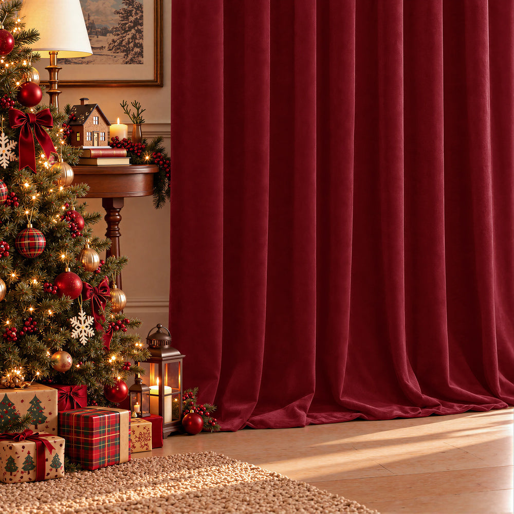 A pair of deep red velvet curtains hanging in a styled living room next to a brown leather armchair, with a lamp, side table, and wood floor visible.