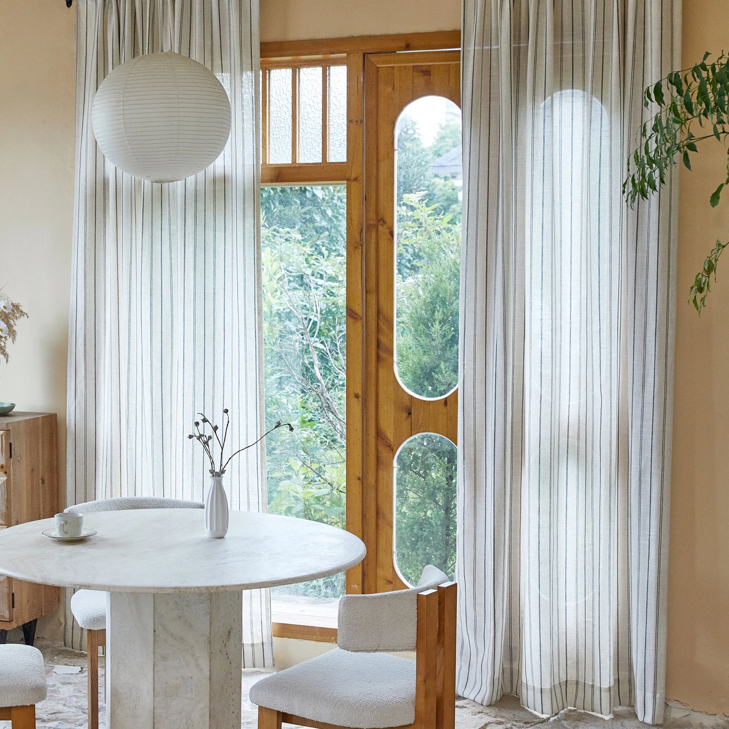 Dining room with round table and chairs, windows framed by farmhouse linen curtains with asymmetrical charcoal stripes.