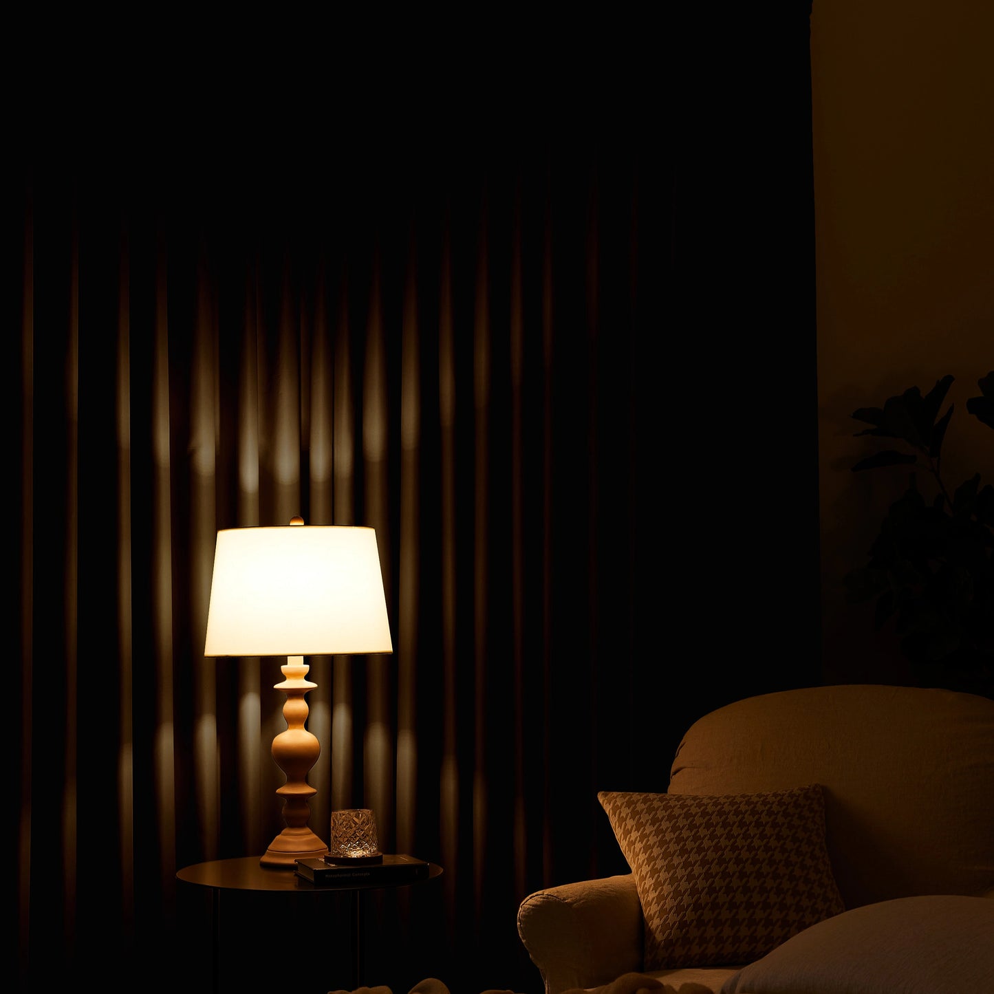Lamp on a table next to a chair with a greige curtain in the background