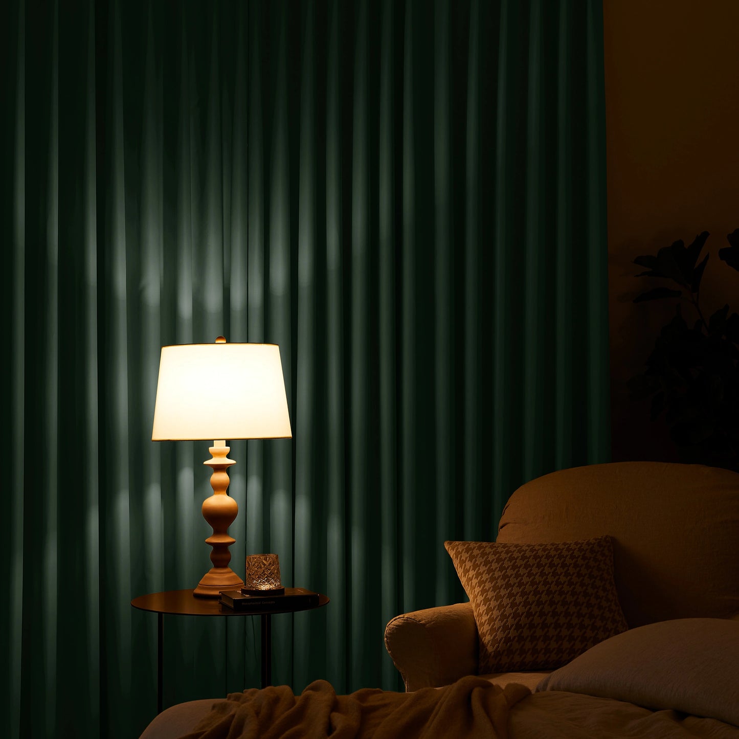 Lamp on a table next to a sofa with dark green curtains in the background