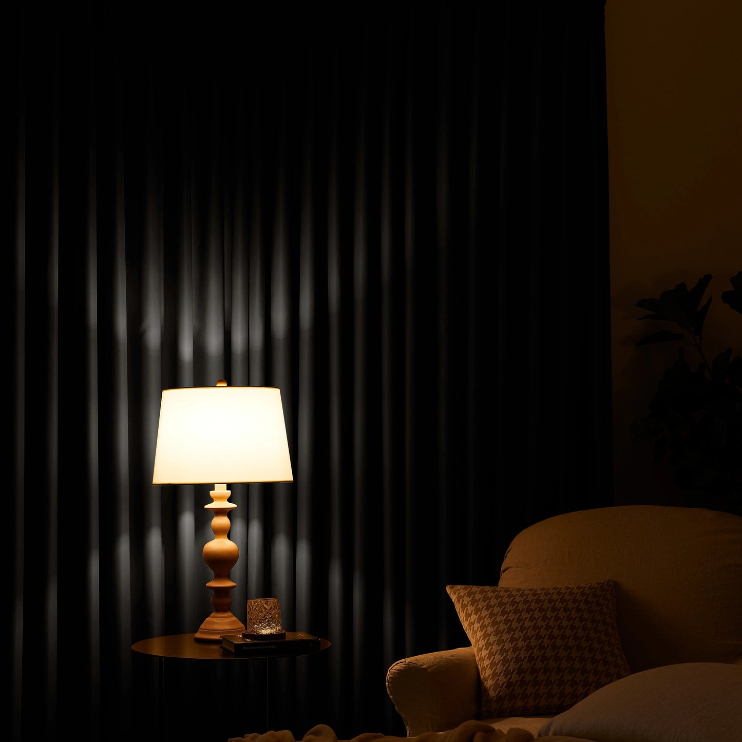 Lamp on a table next to a chair with a neutral gray curtain in the background
