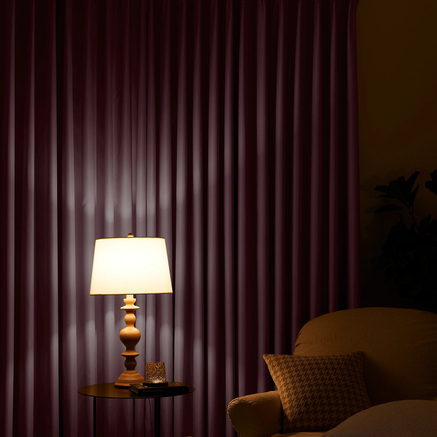 Lamp on a table next to a chair with a muted pink curtain in the background