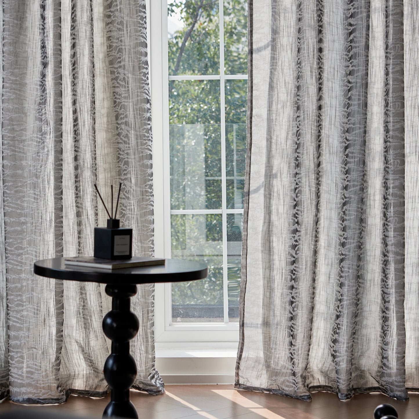 Iron-gray contemporary curtains at a window with a black round table and reed diffuser in front.