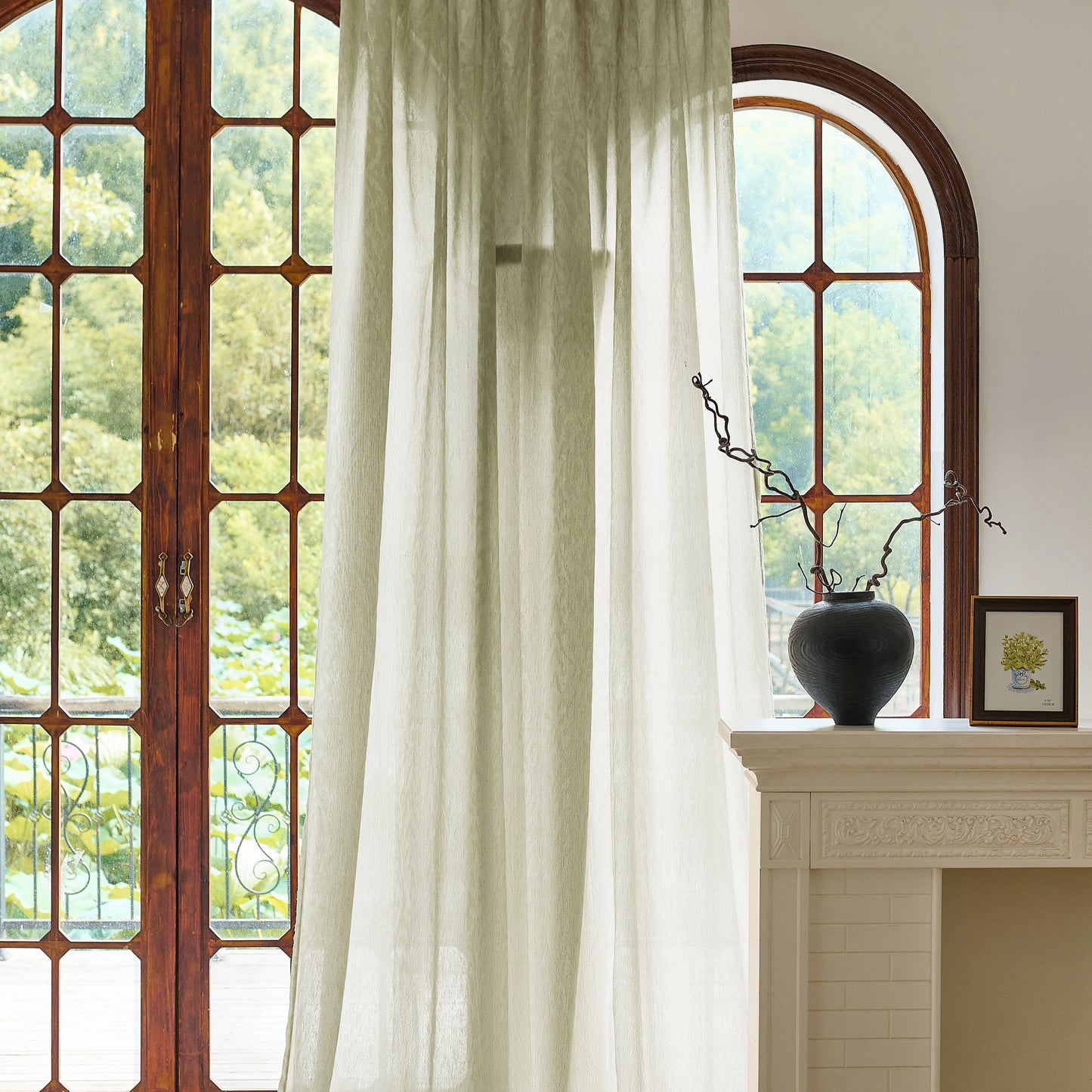 Green curtains in front of a large window with a decorative vase on a mantelpiece.