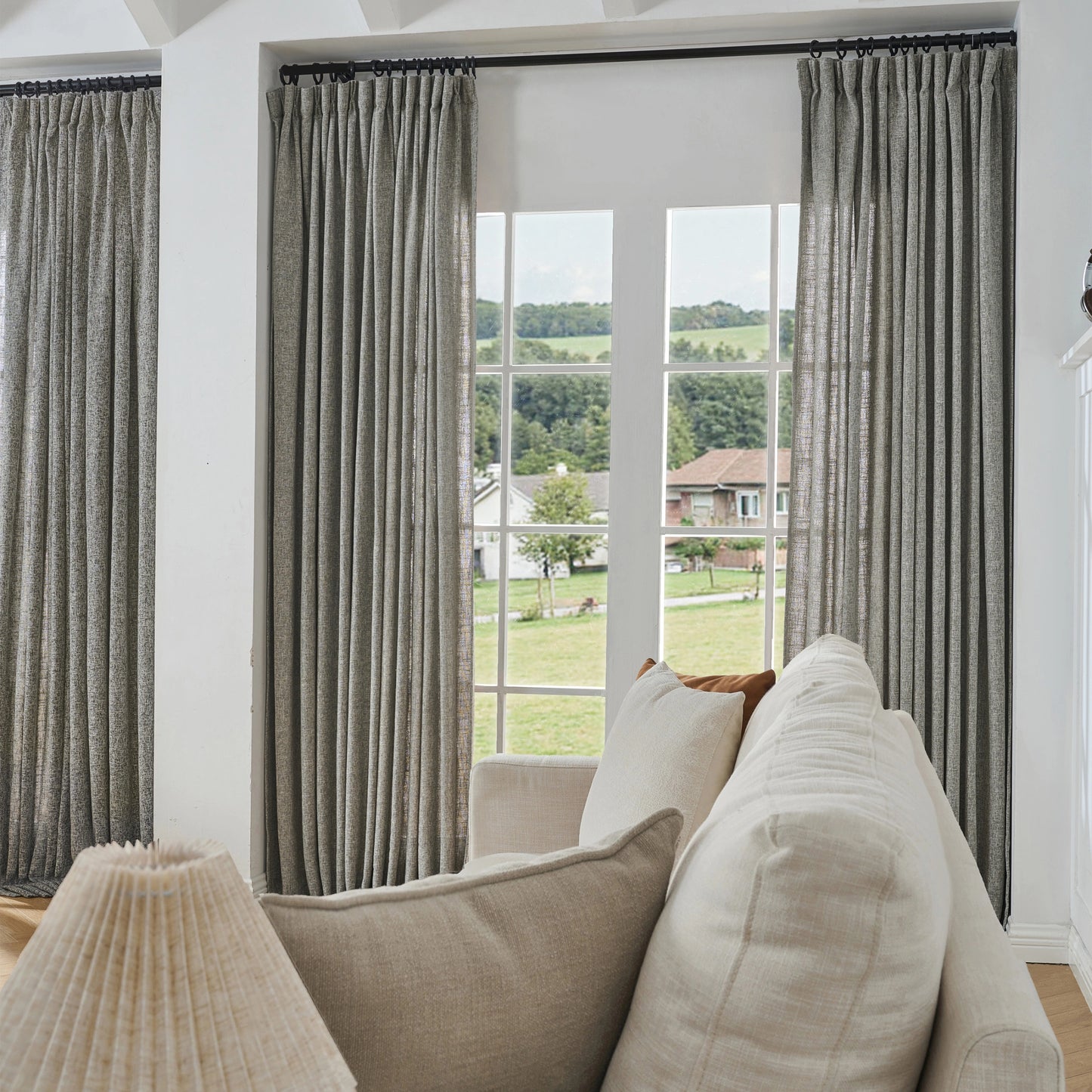 Natural gray poly viscose linen window drapes, soft curtains and a sofa in a room with a large window view.