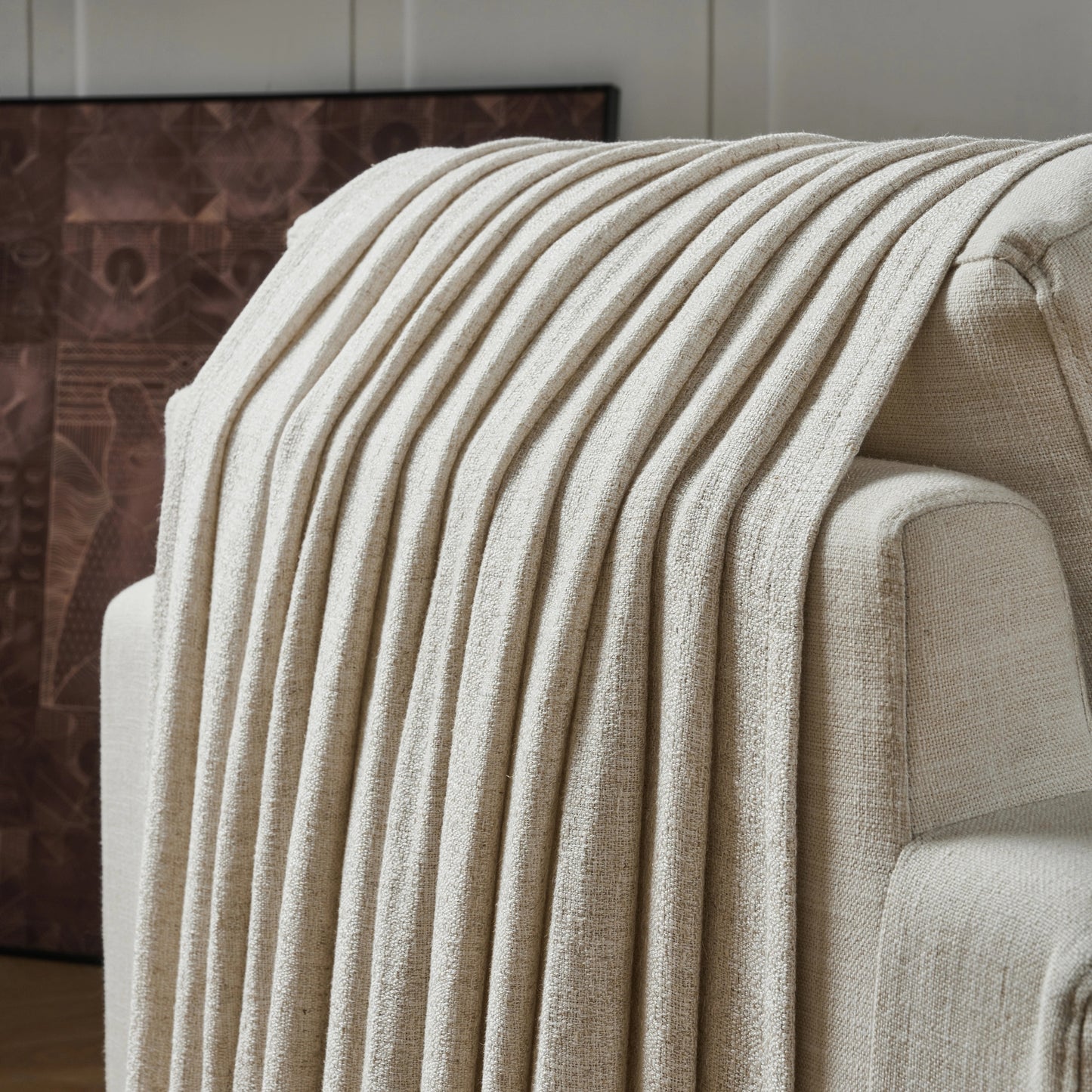 Cream textured curtain draped over a sofa, with a decorative wall in the background.