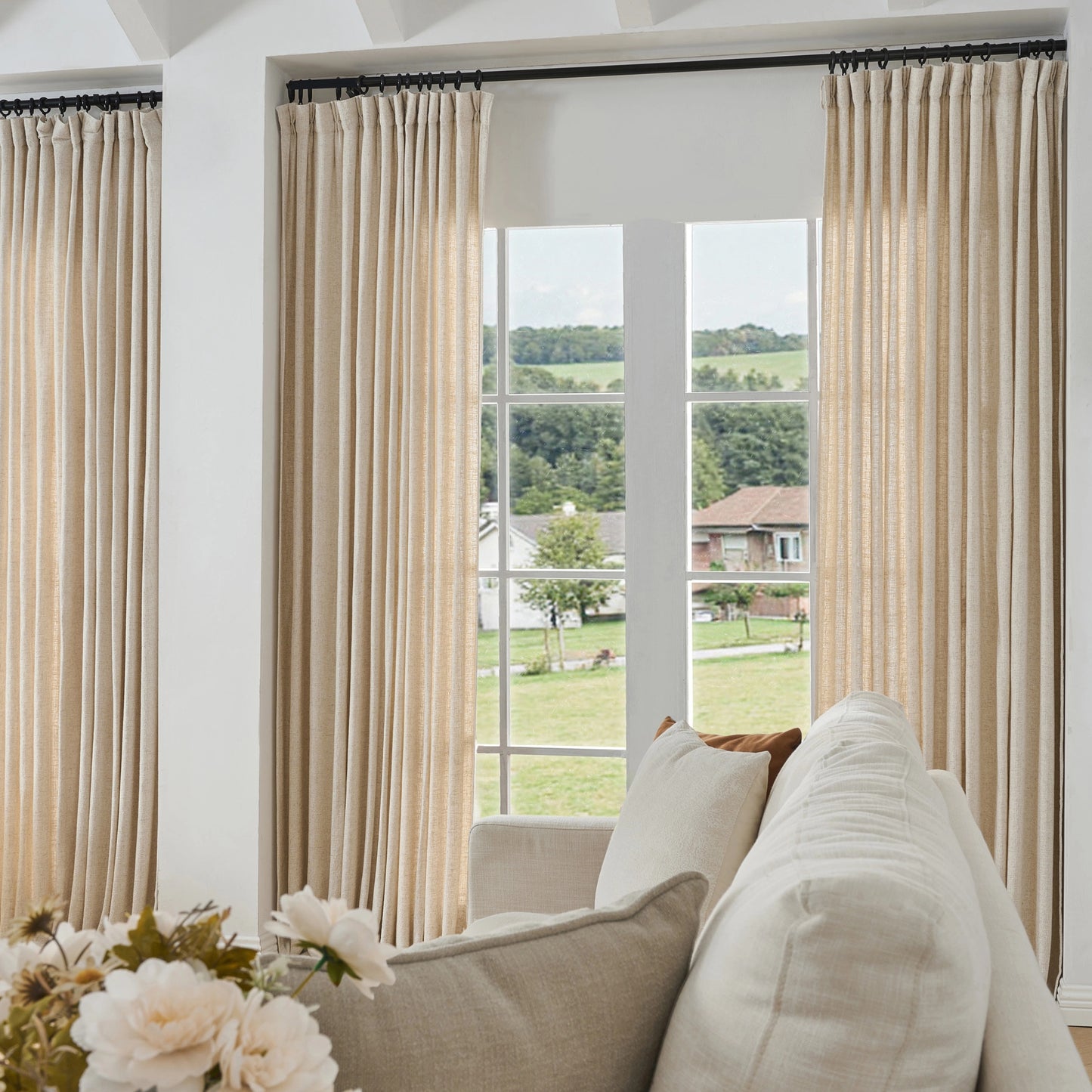 Living room with eggshell-colored curtains made of viscose, polyester, and linen, a sofa, and a view of greenery outside.