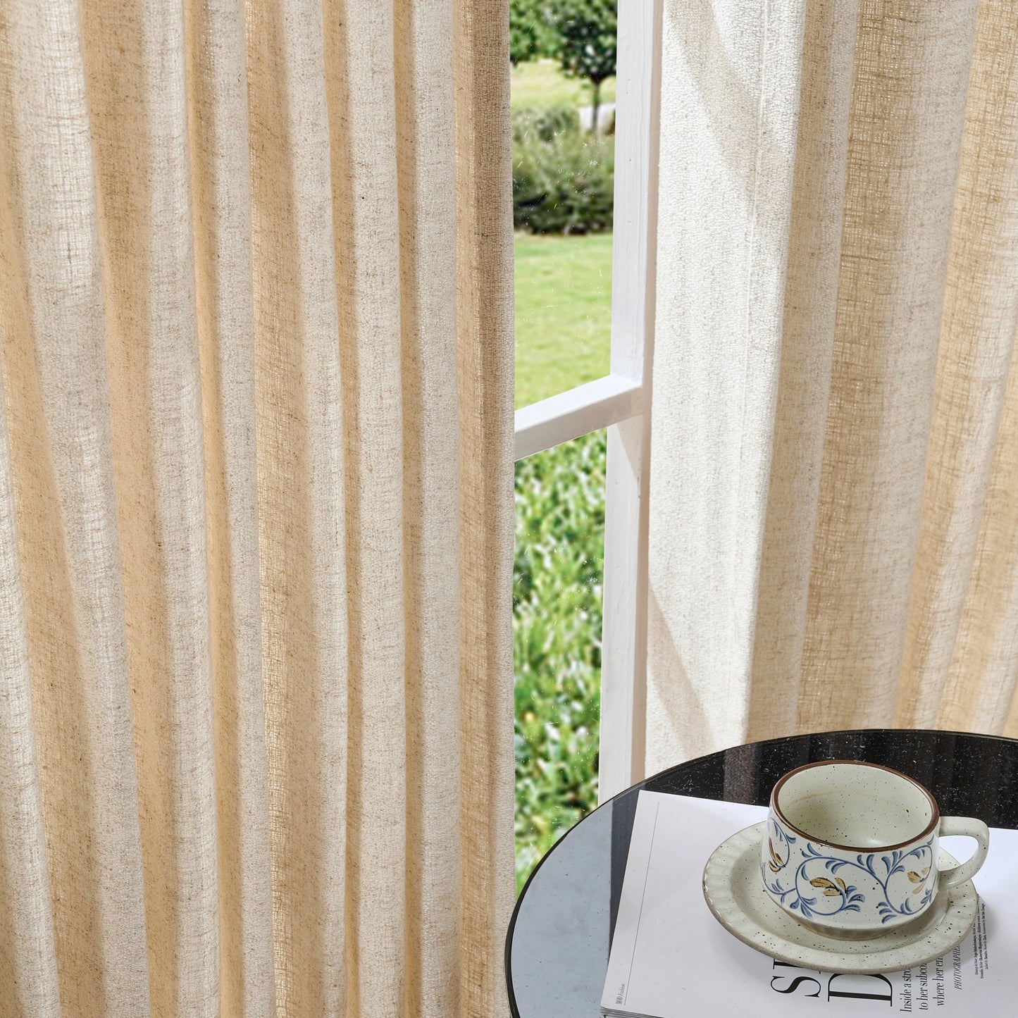 Natural ivory curtains made of viscose, polyester, and linen, with a cup and saucer on a table in the foreground.