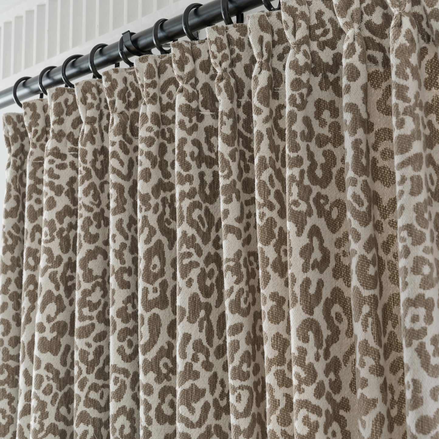 Pleated leopard print curtain panel with stylish folds, hung using pinch pleat method.