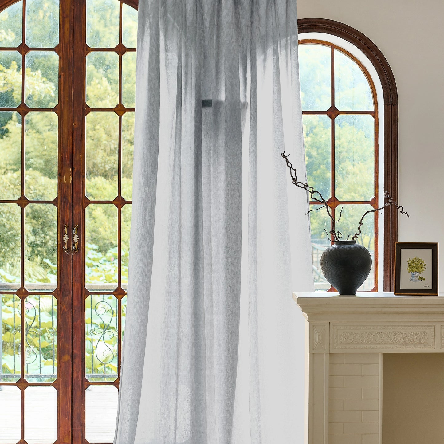 gray sheer in front of a large window with a vase on a mantelpiece.