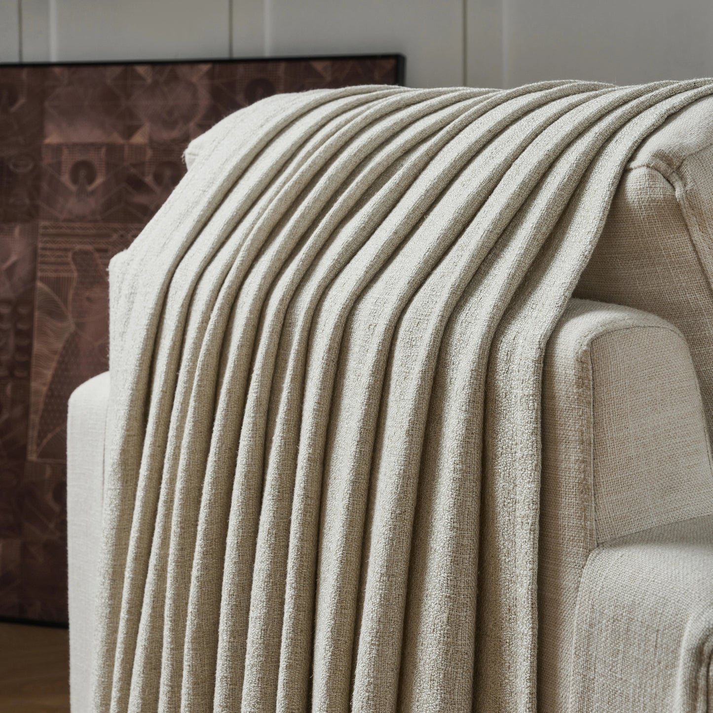 Light camel textured curtain draped over a sofa, with a decorative wall in the background.