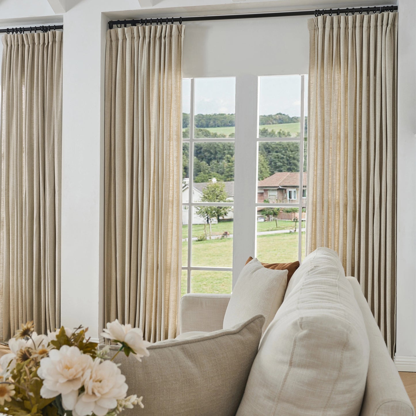Living room with beige camel curtains made of viscose, polyester, and linen, a sofa, and a view of greenery outside.