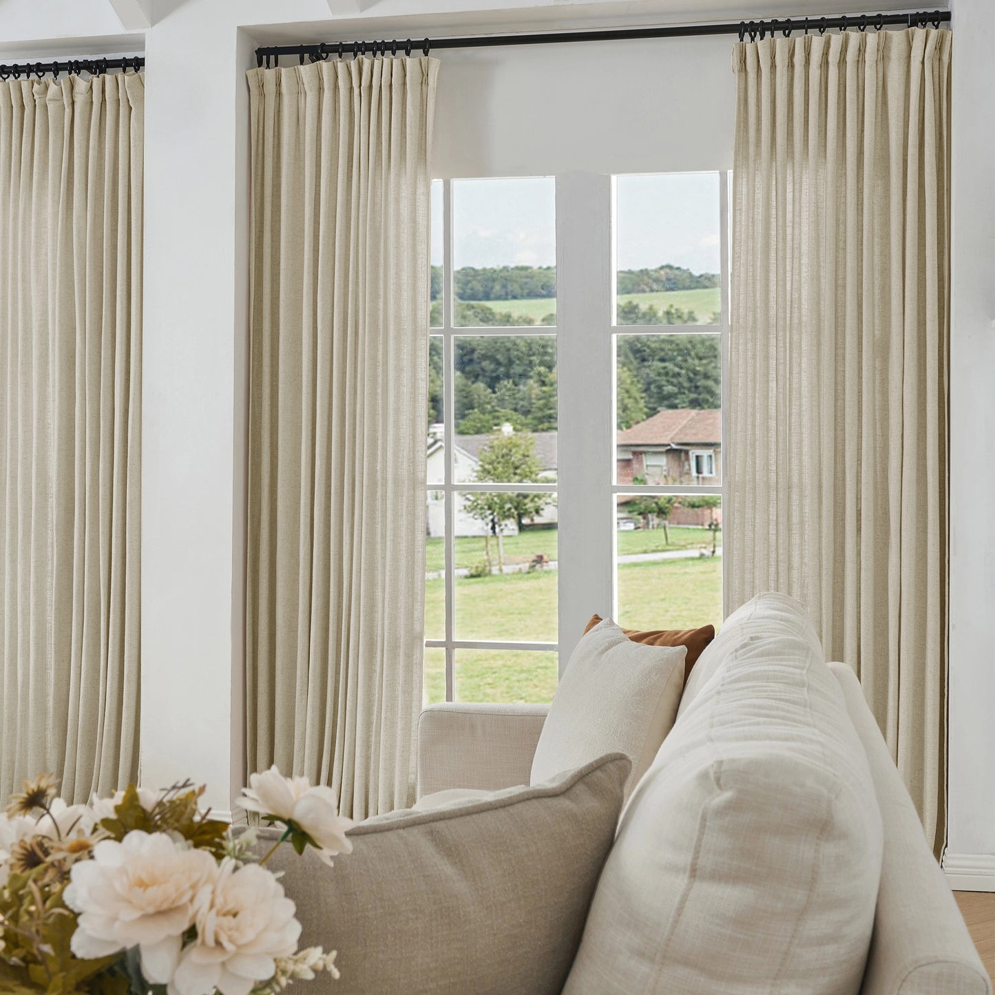 Living room with eggshell ivory curtains made of viscose, polyester, and linen, a sofa, and a view of greenery outside.