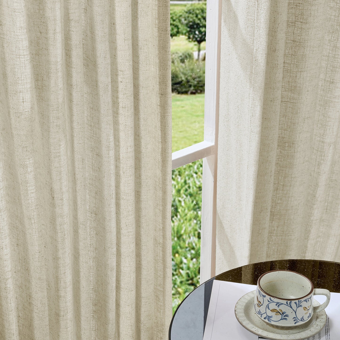 Soft ivory curtains made of viscose, polyester, and linen, with a cup and saucer on a table in the foreground.