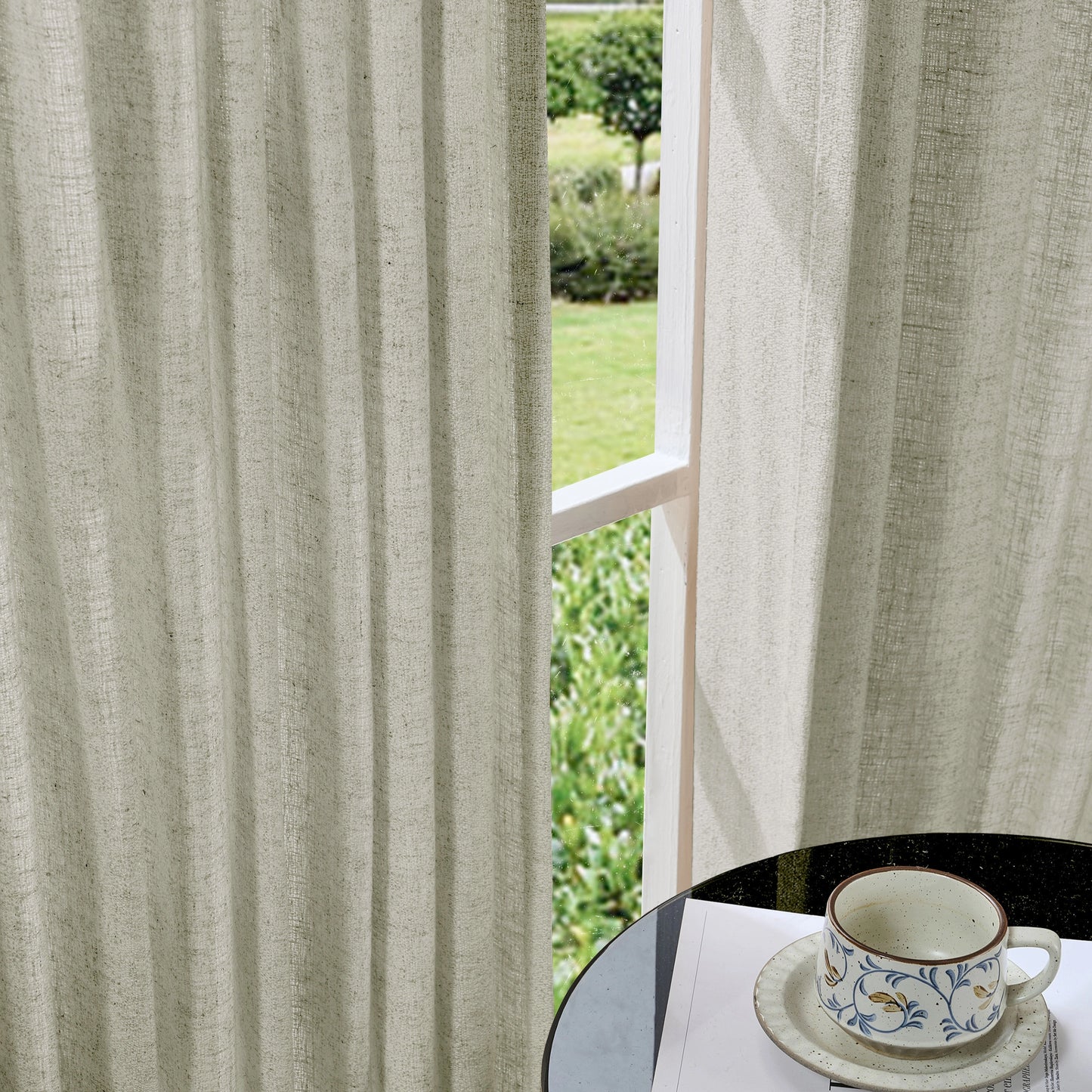Soft ash gray curtains made of viscose, polyester, and linen, with a cup and saucer on a table in the foreground.