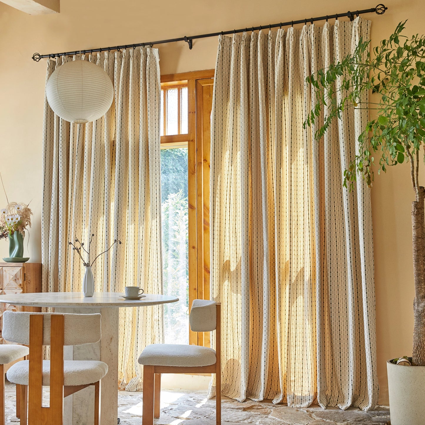 Dining room with sand-colored polyester modern drapery featuring embossed black line design, with table and chairs in front.