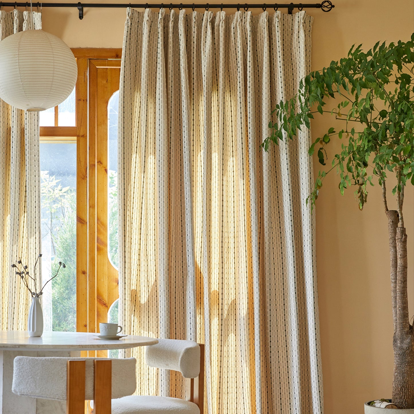 Taupe modern polyester curtain with raised black linework behind a dining table, chairs, and a plant.