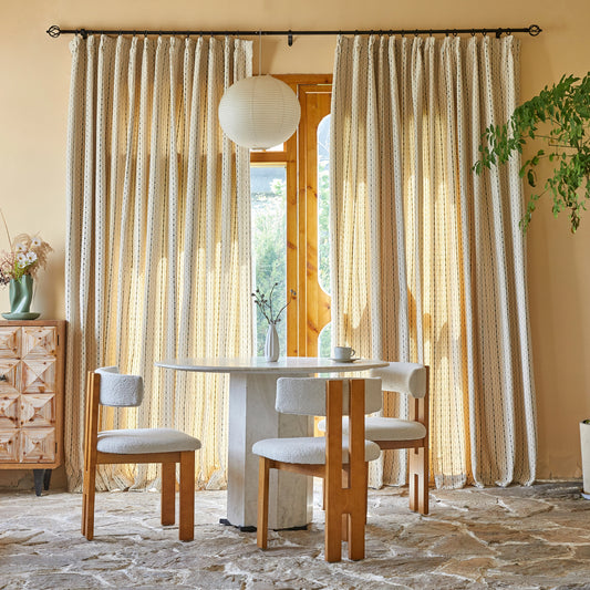 Dining table and chairs in front of tan polyester modern curtains with raised black linear pattern.