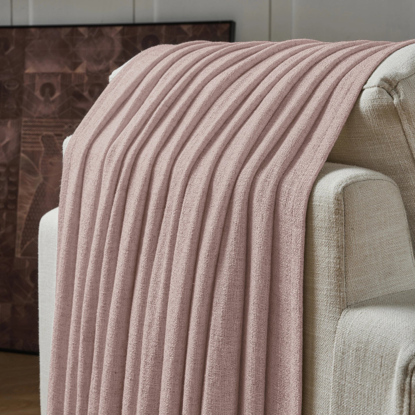 Muted pink textured curtain draped over a sofa, with a decorative wall in the background.