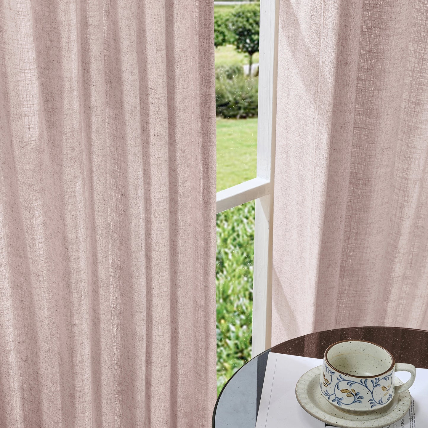 Soft rose pink curtains made of viscose, polyester, and linen, with a cup and saucer on a table in the foreground.