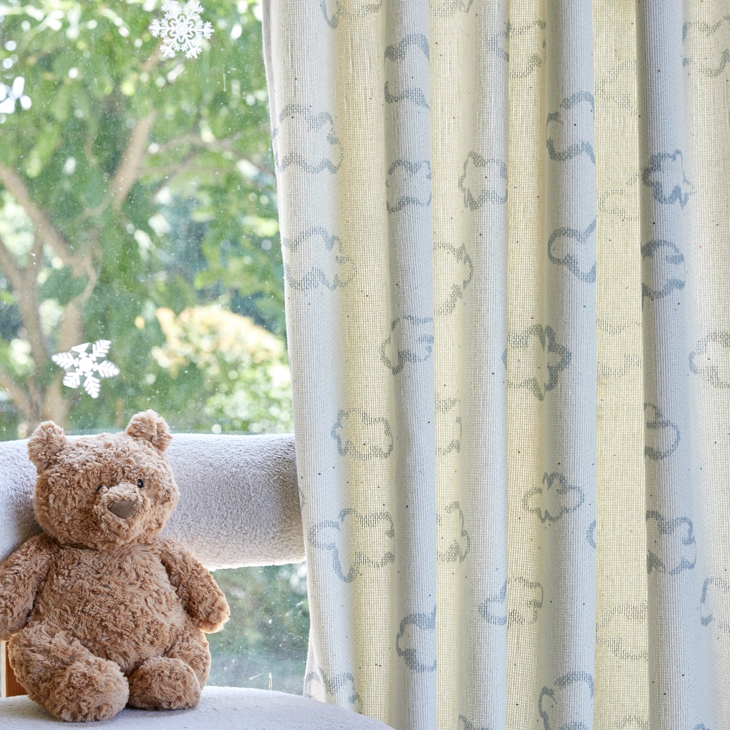 Teddy bear sitting on a chair with playful blue line white cloud patterned textile, with greenery outside.