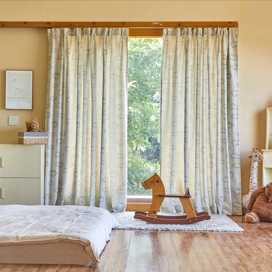 Playful drapery with blue line white cloud motif, in a room with a bed, a small wooden horse, and some children's toys.