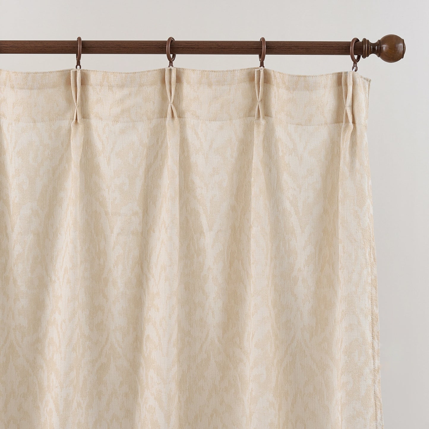 Beige curtain with wooden rod and hooks on a plain background