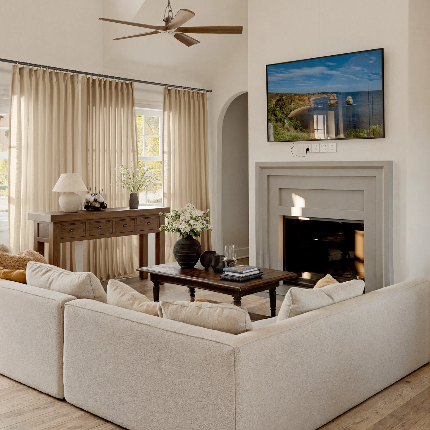 Living room with ecru curtains, beige sofa, coffee table, and TV mounted on the wall.