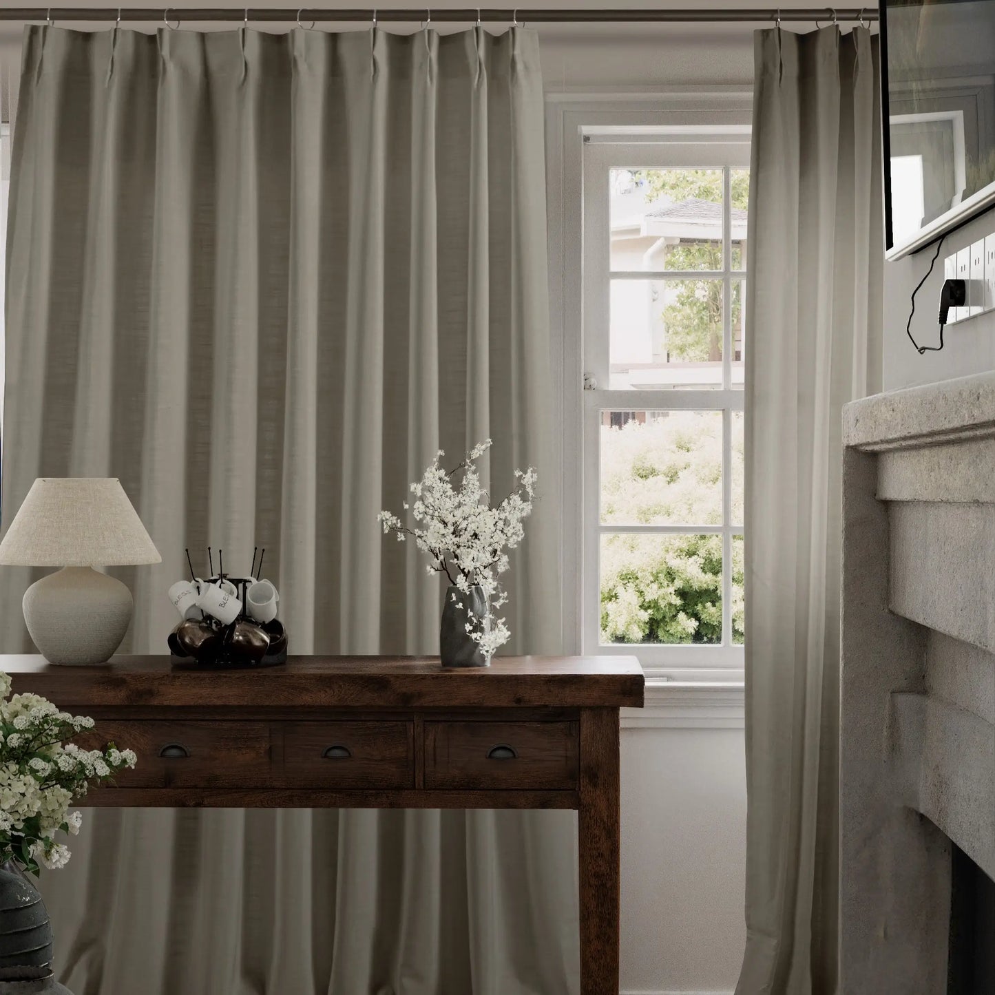 Living room with greige curtains, wooden console table, lamp, and curtains.