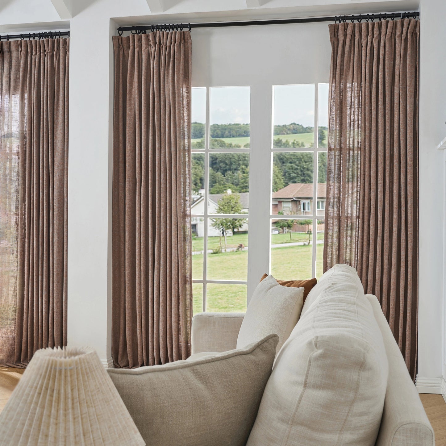 Muted reddish brown poly viscose linen window drapes, soft curtains and a sofa in a room with a large window view.