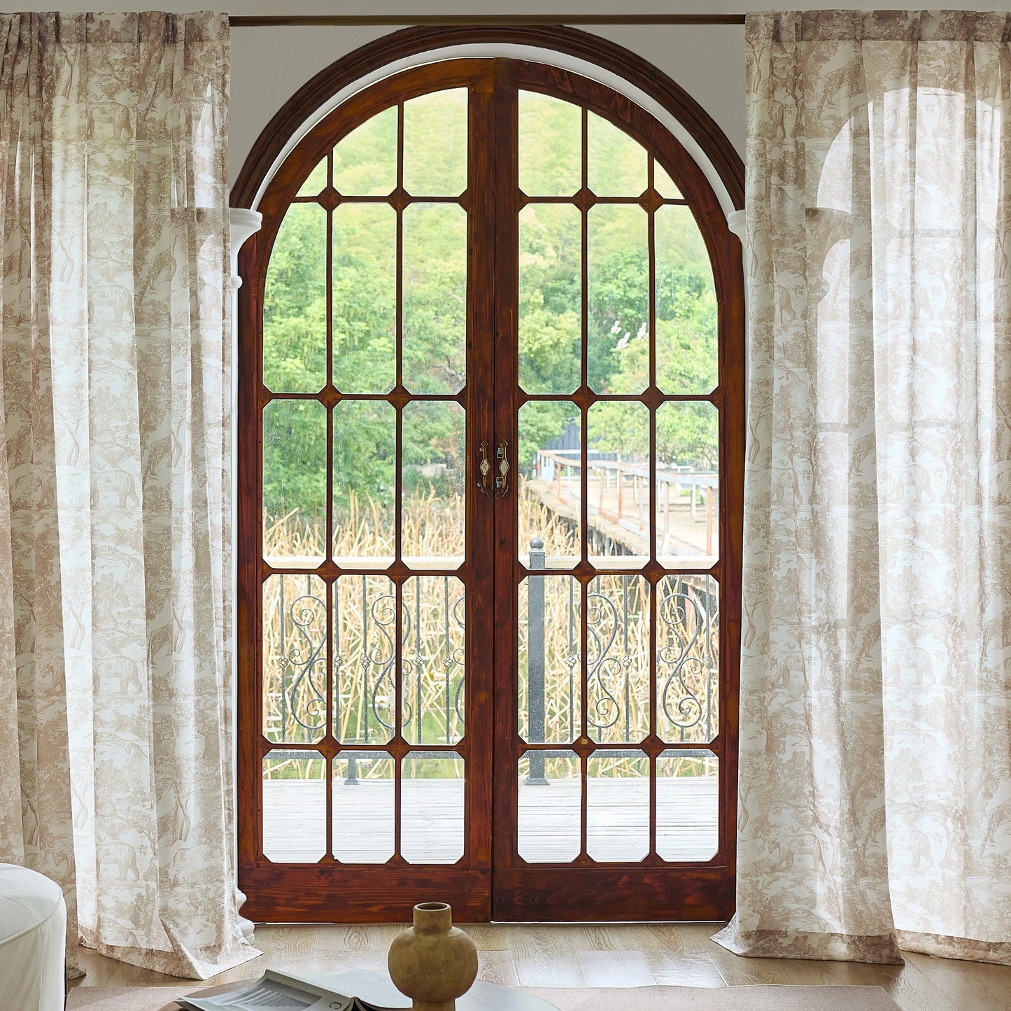 Living room styled with chestnut toile sheer back tab curtains, with lush greenery visible outside.