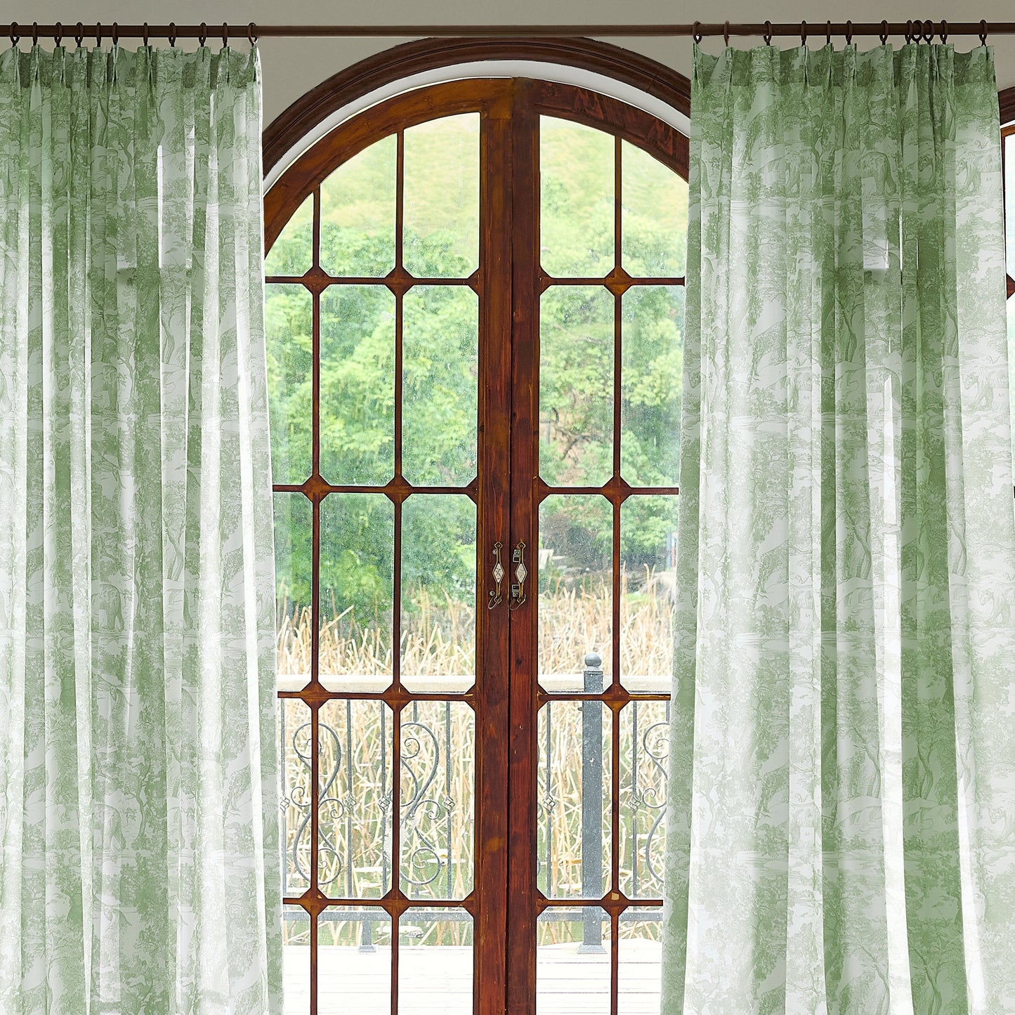 Green toile sheer curtains softly filtering natural light, framing an arched window with an airy and elegant look